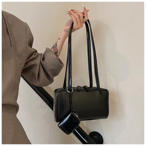 Detail of glossy black shoulder bag with thin straps and a matching mini pouch