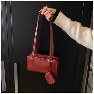 Close-up of burgundy glossy leather shoulder bag with matching mini charm and silver zipper