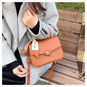 Close-up of caramel leather crossbody bag with woven texture and decorative silk scarf