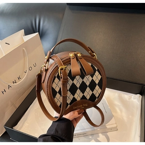 Detail of checkered round bag featuring brown leather trim and dual metal zippers