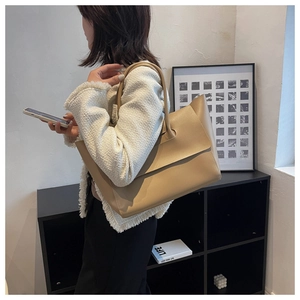Minimalist beige leather tote bag shown on model in a modern interior setting