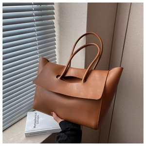 Close-up of caramel brown leather tote bag with unique flap handle design in hand