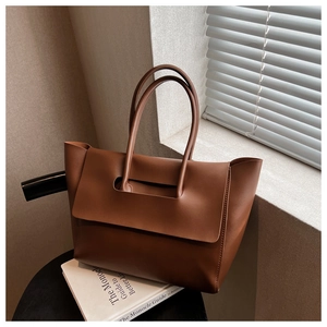 Detailed view of deep brown matte leather tote bag handle and flap design in natural light
