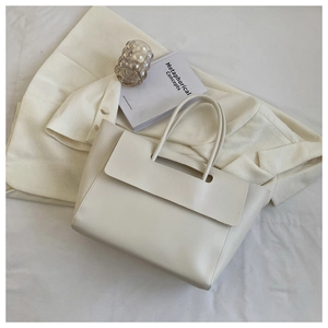 Overhead view of a minimalist cream-white tote bag with a flap closure on a styled desk