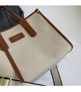 Detail of canvas tote bag with leather trim and fashion brand tag on beige fabric