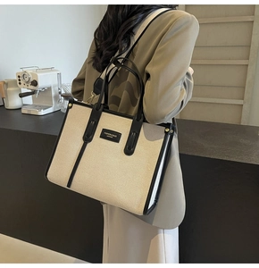 Detail of canvas tote bag with black leather handles and shoulder strap on a model