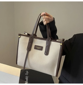 Detail of canvas tote bag with brown leather trim and fashion lettering logo plaque