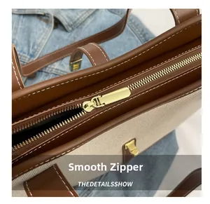Close-up of smooth gold zipper and white stitching on canvas tote bag with leather trim