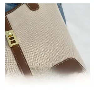 Detail of canvas tote with brown leather trim, gold metal clasp and white stitching