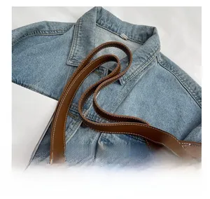 Detail of dark brown leather handle on cream canvas tote bag with contrast stitching