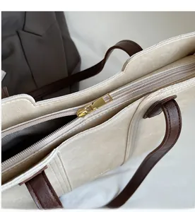 Close-up of smooth gold metal zipper and leather strap on a beige tote handbag