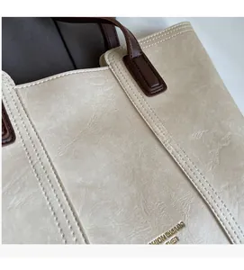 Macro view of beige textured leather tote with contrast stitching and gold foil logo
