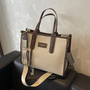 Minimalist canvas tote bag with brown leather trim and adjustable strap on a sofa