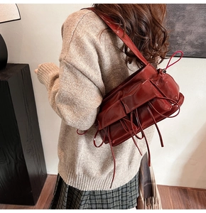 Détail du sac à épaule en cuir verni bordeaux avec franges et glands décoratifs