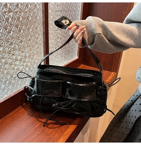 Détail d'un sac à épaule en cuir verni noir avec nœuds et poches 3D tenu à la main