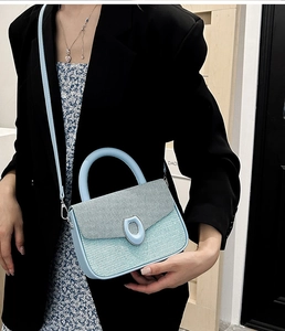Detail of light blue textured crossbody bag with metallic clasp worn by a model
