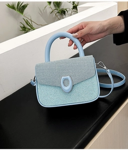 Detail of light blue textured crossbody bag with silver buckle and woven finish