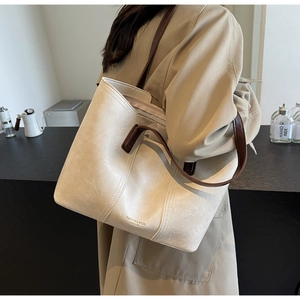 Close-up of cream leather tote bag with brown straps and logo detail for daily commute