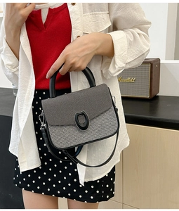 Detail of tweed and black leather shoulder bag with oval buckle held by a model