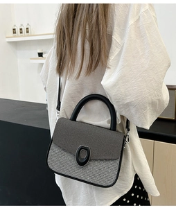 Detail of gray woven texture shoulder bag with black leather strap and round metal clasp
