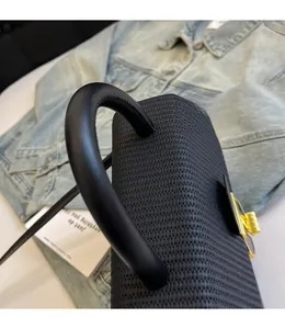 Close-up of black woven leather handbag with sturdy top handle and gold metal twist lock
