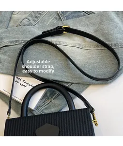 Detail of adjustable leather strap and gold-tone buckle on woven black crossbody bag