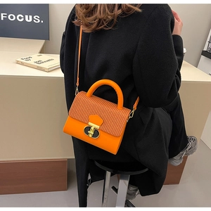Detail of bright orange crossbody bag with woven flap and metallic turn-lock closure
