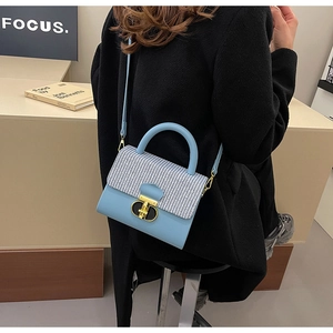 Detail of blue leather bag with houndstooth flap and gold clasp held by a model