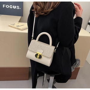 Detail of cream crossbody bag featuring a woven flap and elegant gold hardware