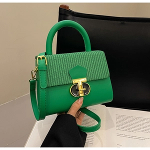 Close-up of green leather handbag featuring woven texture flap and golden swivel clasp