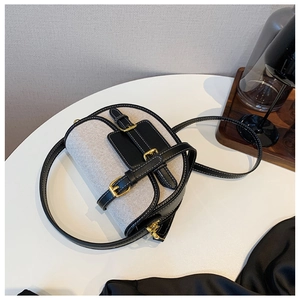 Detailed view of canvas and black leather saddle bag with gold buckles and contrast stitching