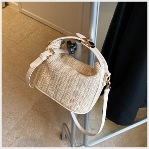 Detailed view of woven straw handbag with white leather trim and golden metal lock buckle