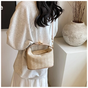 Detail shot of straw woven crossbody bag featuring leather straps and golden metal hardware