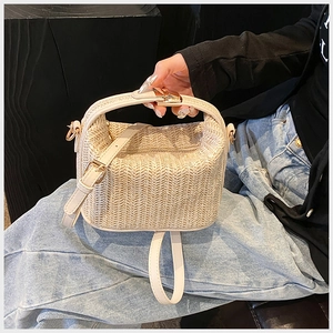 Detail of beige woven straw tote bag with brown leather strap and gold metal hardware