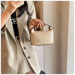 Detail of handwoven straw tote bag with brown leather trim and golden hardware