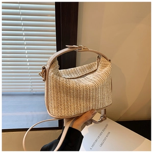 Detail of beige straw handbag featuring V-pattern weave and elegant metal clasp closure