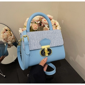 Light blue crossbody bag featuring a woven flap, gold twist lock, and top handle