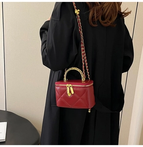 Detail of red quilted mini box bag with gold metal handle and woven chain strap