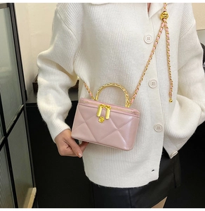 Detailed view of pink quilted vanity box bag with gold metal handle and chain strap