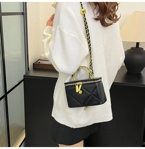 Detail of black quilted chain box bag with gold metal handle and camellia charm