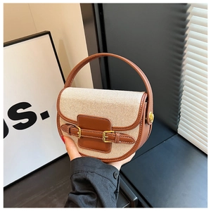 Canvas saddle bag with brown leather trim and gold hardware in a handheld pose
