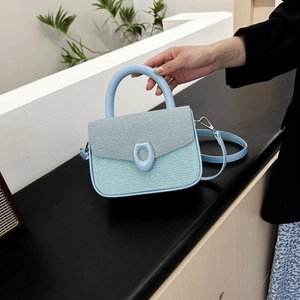 Light blue textured crossbody bag with silver ring clasp shown in hand against white wall