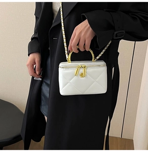 Close-up of quilted white box bag with gold handle and floral zipper charm detail