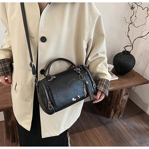 Detail of black leather Boston bag with decorative brown tassel and metallic accents