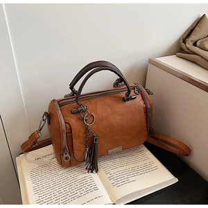 Macro detail of brown leather Boston bag with decorative cat tassel charm and metal zippers
