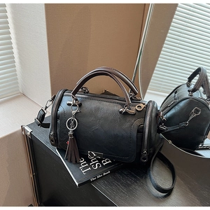 Detail of black Boston bag with pebbled leather texture and decorative tassel accessory