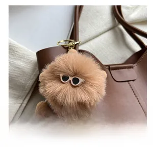 Close-up of a brown plush ball charm with mini sunglasses and gold keychain on a tote bag
