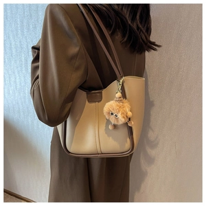 Detail of a beige tote bag with brown trim and plush pompom charm worn by a model
