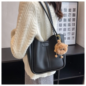 Detail of black matte tote bag featuring vertical stitching and cute plush doll charm