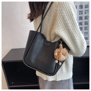 Detail of a black matte tote bag with a brown plush monster charm on a shoulder strap